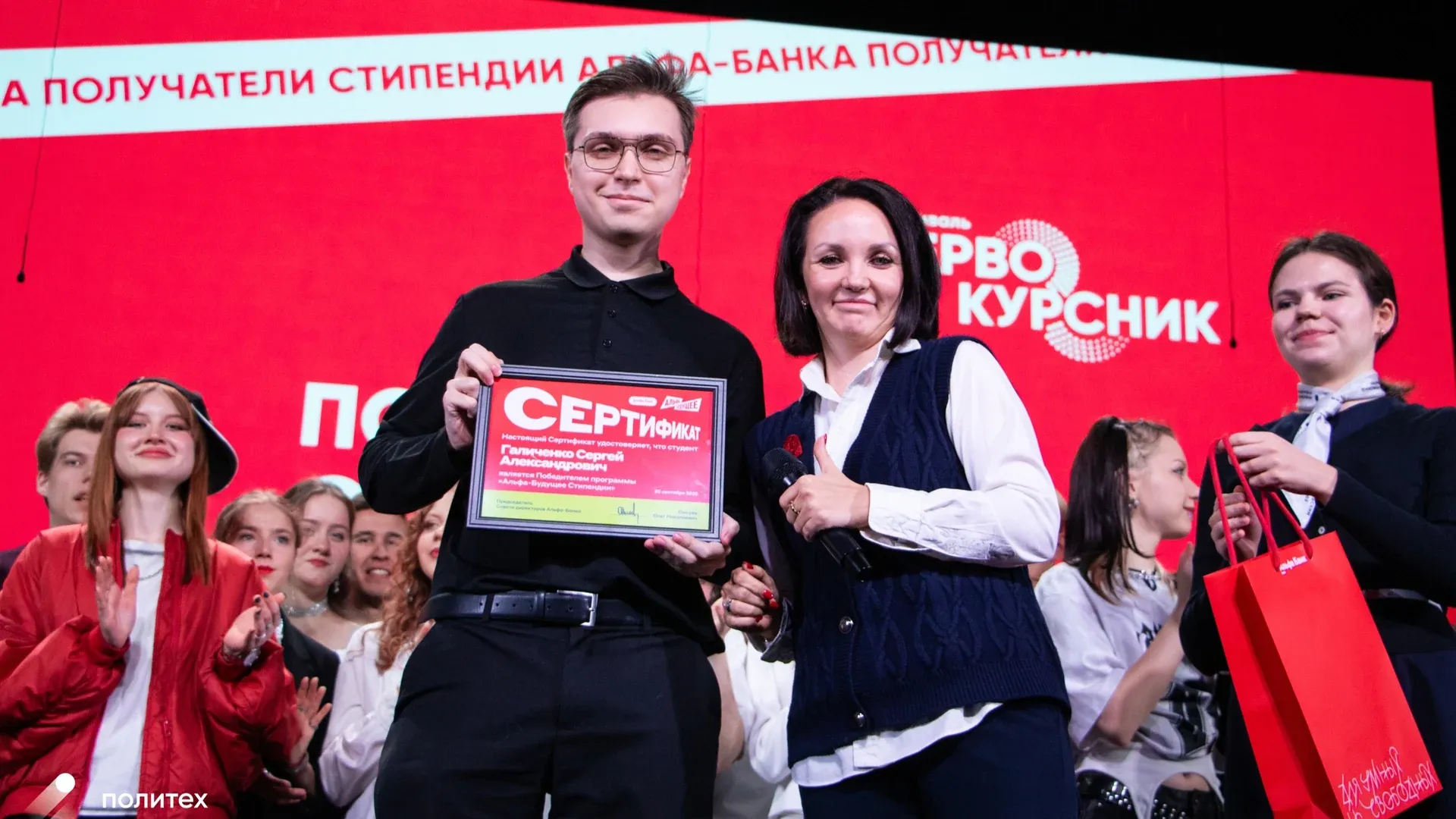 Scholarship certificate presentation on a red-lit stage at Moscow Polytechnic